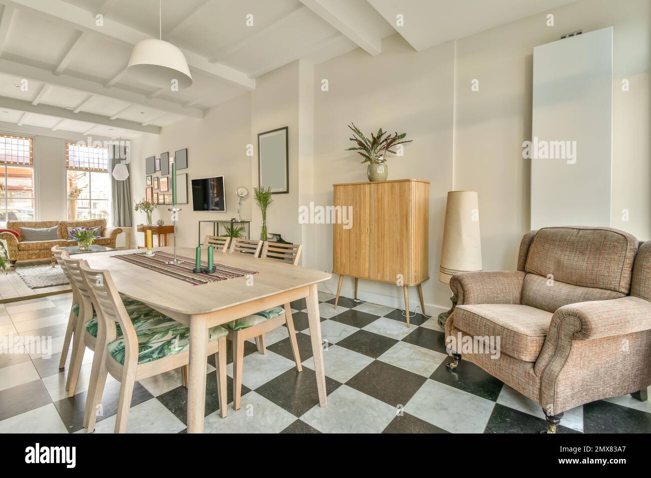 Intérieur de la salle à manger moderne avec table en bois sur les chaises de sol à carreaux avec des plantes vertes imprimé près de fauteuil confortable et des décorations Banque D'Images
