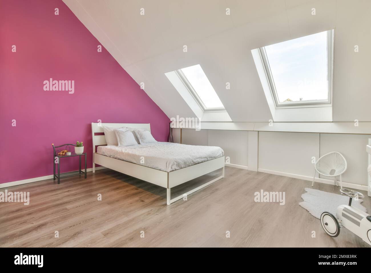 Lit confortable avec coussins et couverture placée contre le mur rose sous les fenêtres de mansarde dans l'intérieur moderne de chambre sur le grenier Banque D'Images
