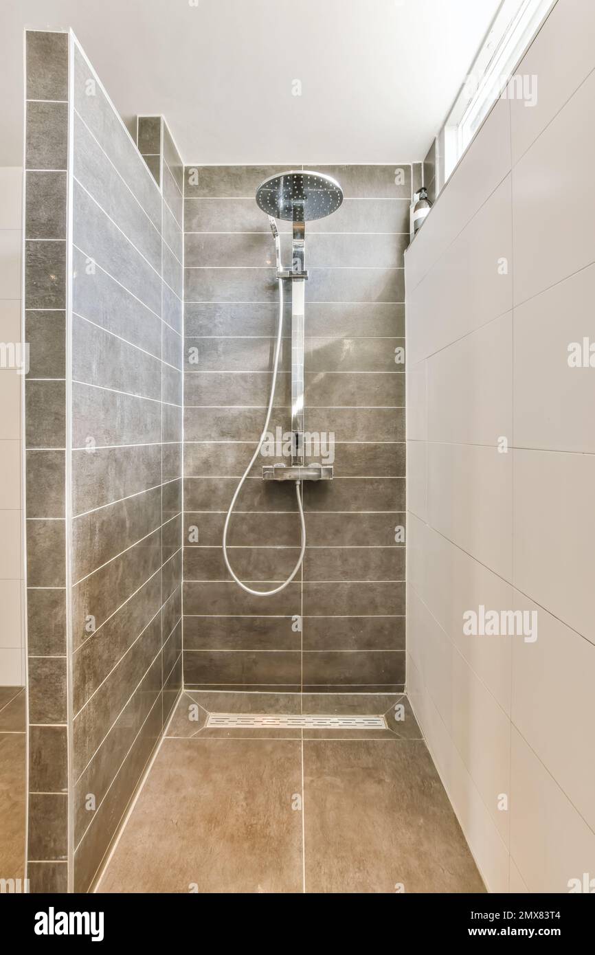 Cabine de douche avec appareils modernes et murs carrelés gris dans la salle de bains contemporaine Banque D'Images