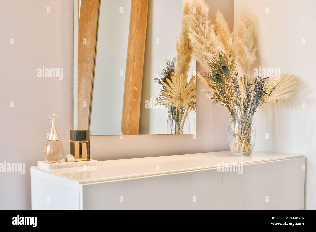 Placard blanc contemporain avec miroir et fleurs décoratives dans un vase placé près des flacons de parfum contre le mur dans un appartement lumineux moderne Banque D'Images