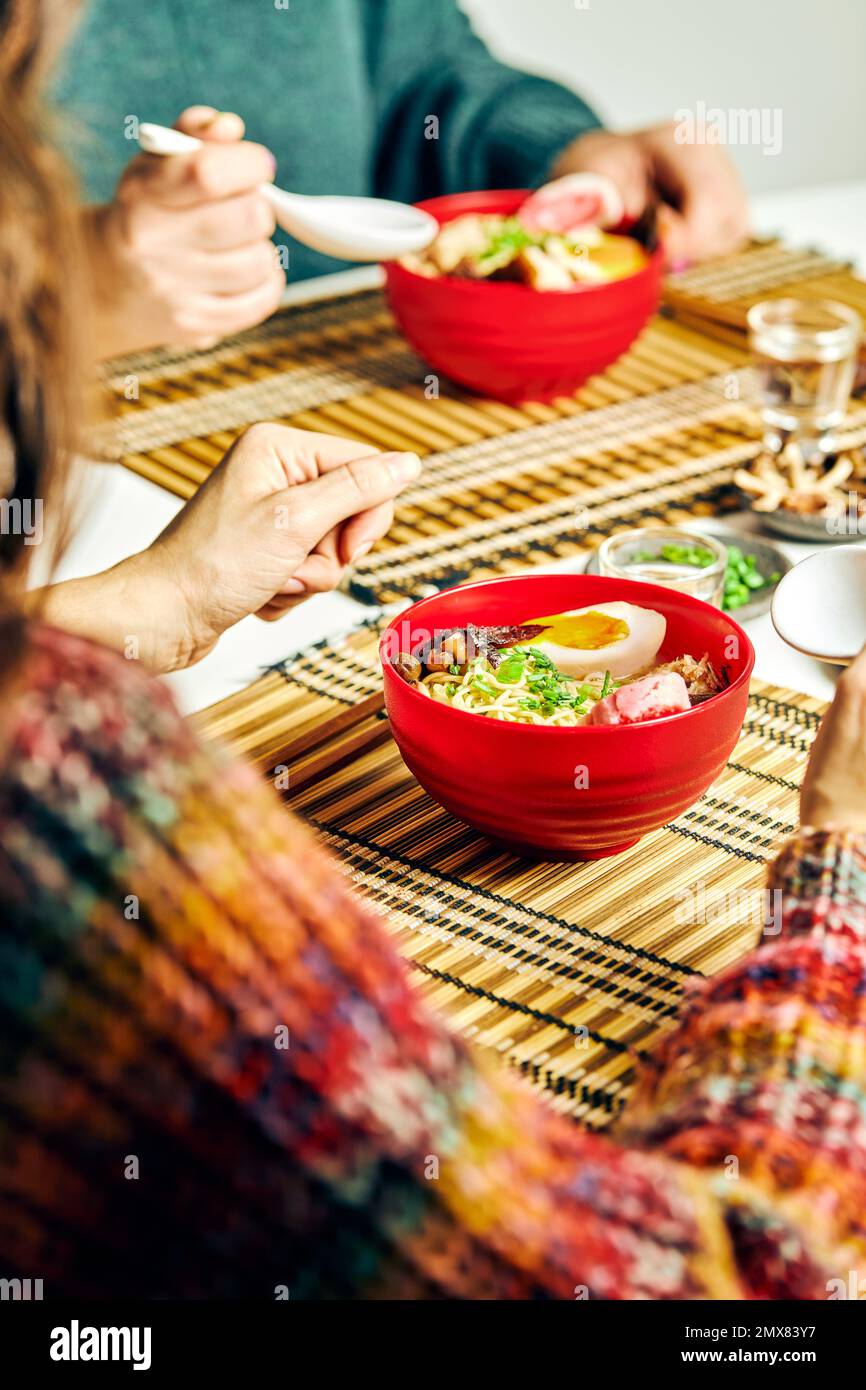 Des personnes méconnaissables s'asseyant à table et mangeant de la soupe de ramen appétissante dans un bol du café Banque D'Images