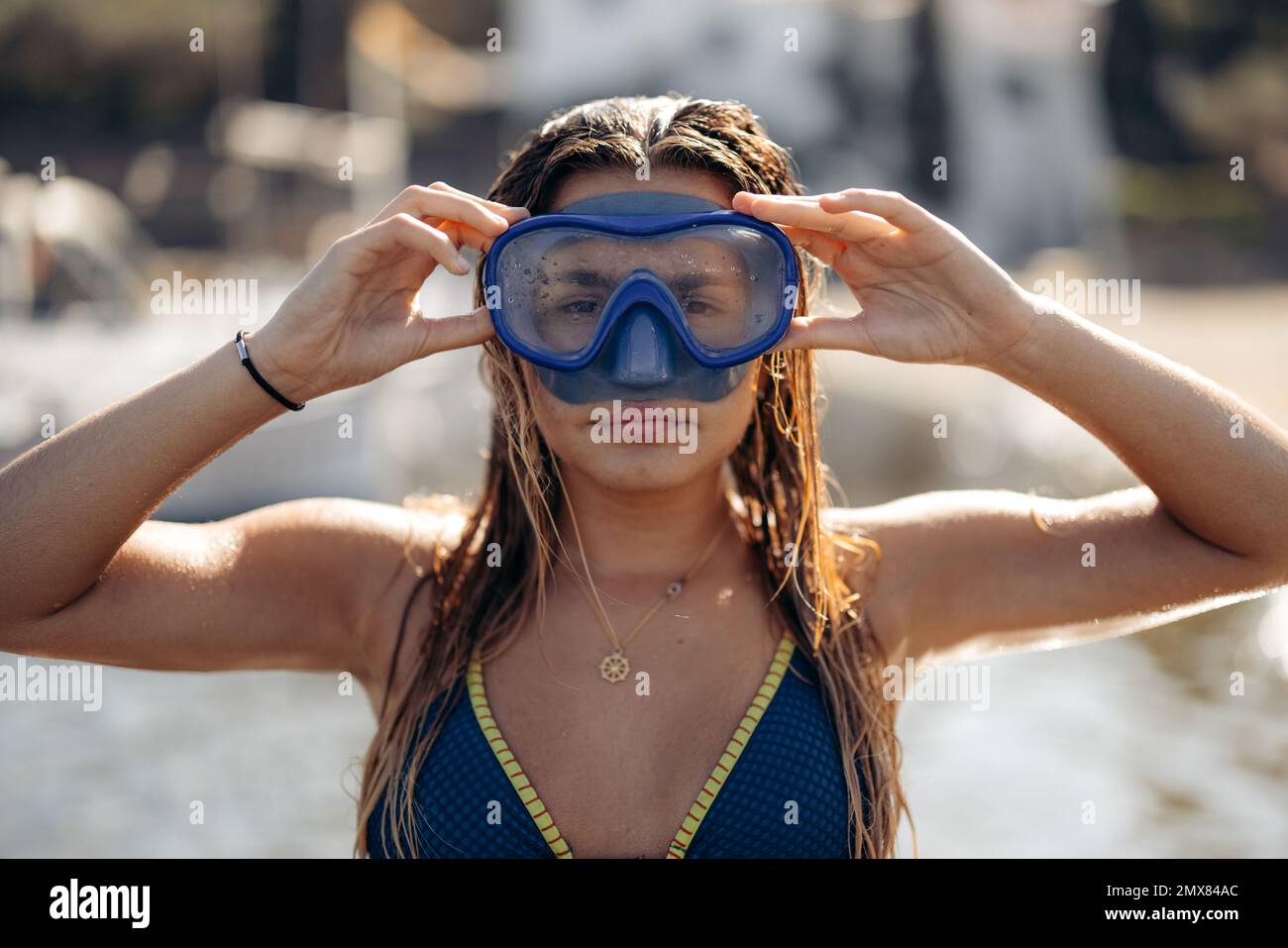 Slim femme plongeur en maillot de bain et lunettes pour plonger sourire et regarder l'appareil photo tout en se relaxant le week-end d'été sur la plage de Cadaques dans le dos éclairé Banque D'Images
