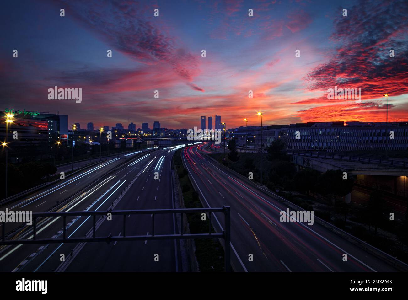 Vue sur la ville au coucher du soleil avec un reflet sur un pont et des traces de lumière des phares des voitures Banque D'Images