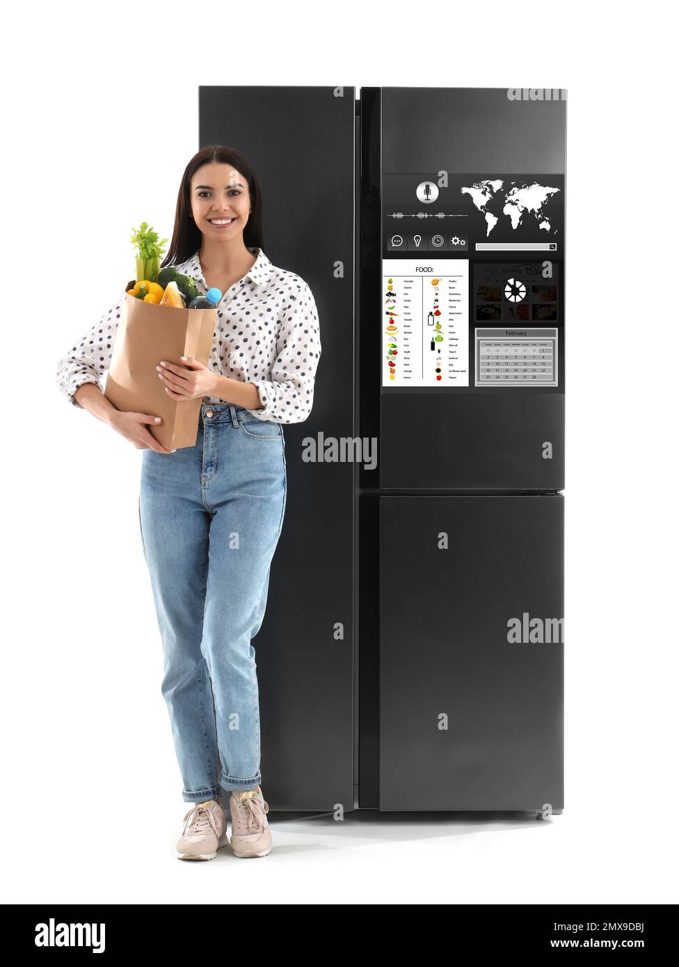 Jeune femme avec sac d'épicerie près d'un réfrigérateur intelligent sur fond blanc Banque D'Images