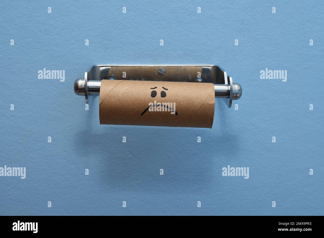 Un rouleau de toilette en carton brun au visage triste a épuisé de papier/mouchoirs de toilette, sur un fond de mur bleu clair au milieu du cadre Banque D'Images