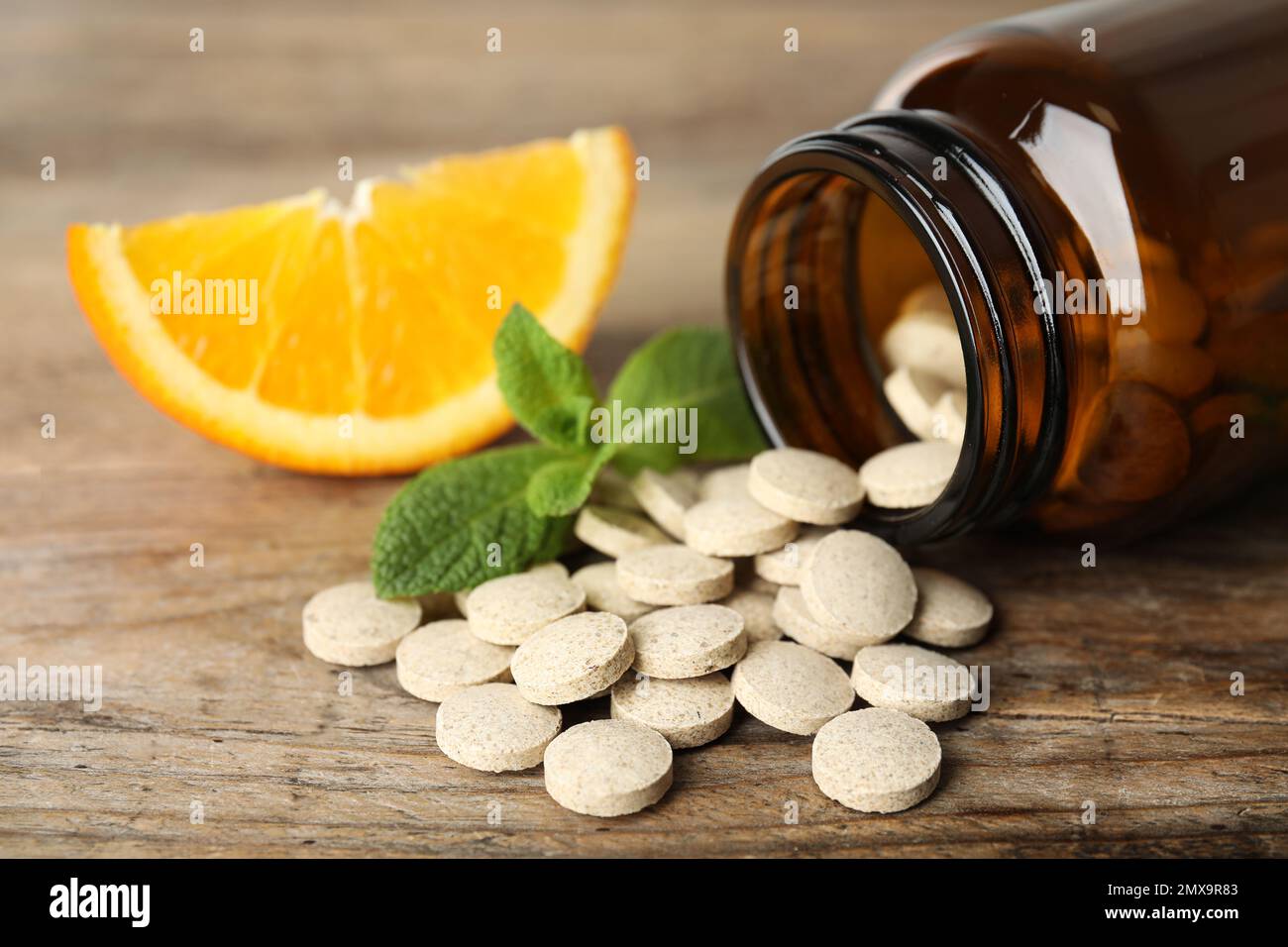 Bouteille avec pilules de vitamine, menthe et orange sur table en bois, gros plan Banque D'Images