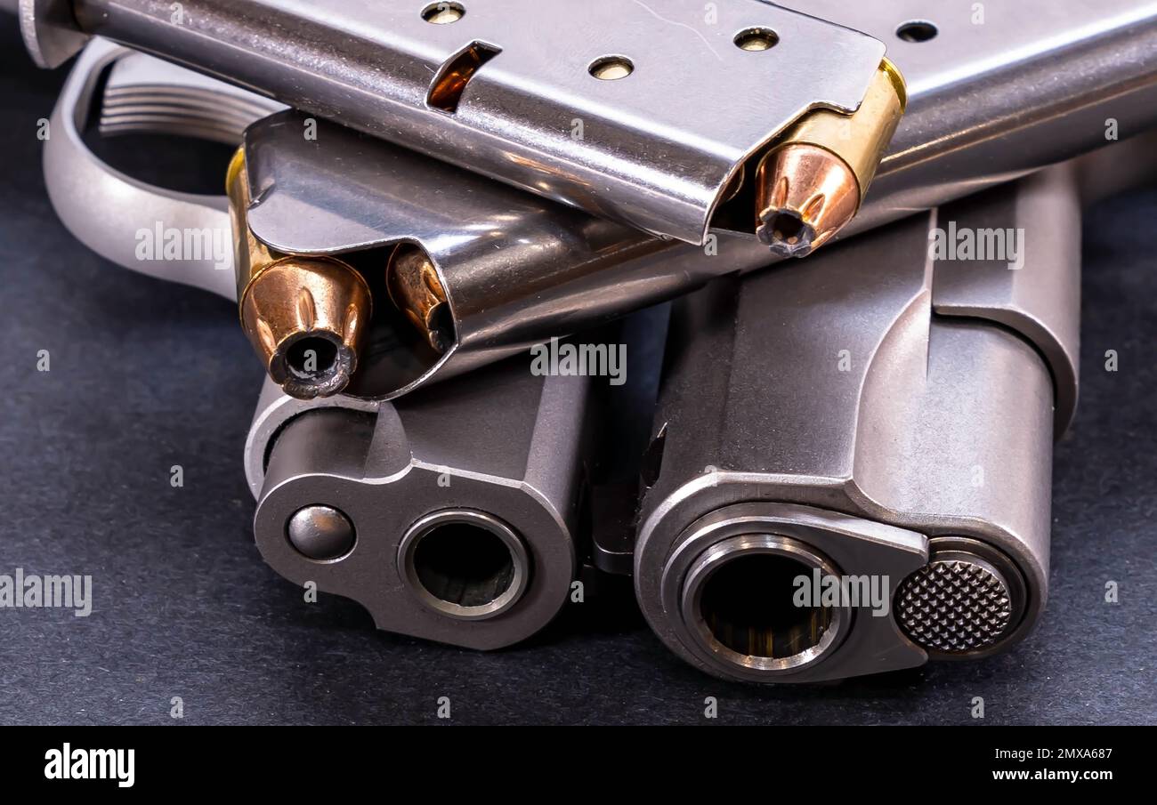 Deux pistolets en acier inoxydable 1911, l'un a 45 ACP et l'autre un calibre 380 avec un chargeur chargé pour chacun sur un fond noir Banque D'Images