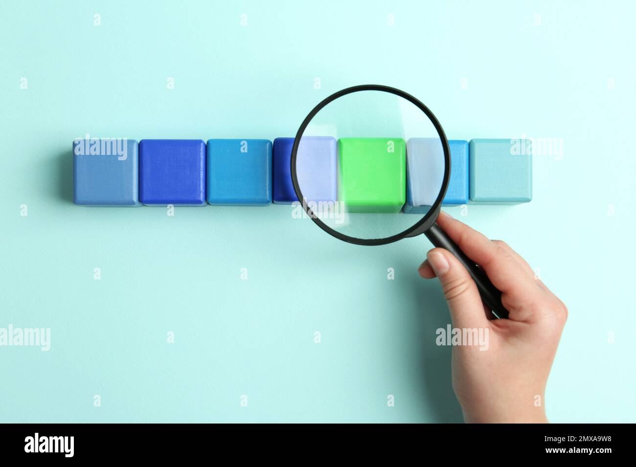 Femme tenant une loupe au-dessus des cubes colorés sur fond bleu clair, vue de dessus. Concept de recherche Banque D'Images