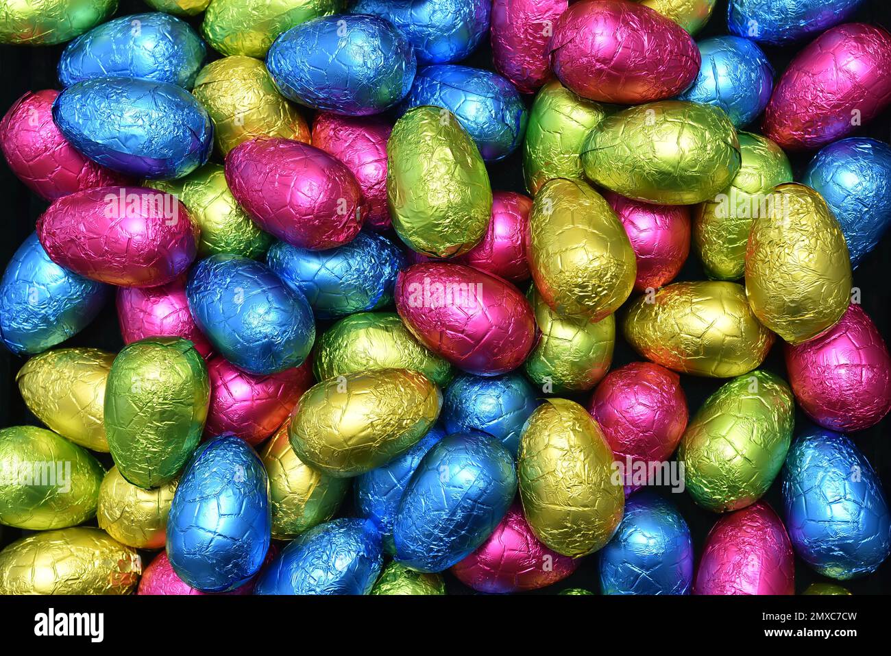 Pile ou groupe d'œufs de pâques en papier d'aluminium multicolore enveloppés de chocolat dans des tons de rose, bleu, jaune et vert lime. Banque D'Images