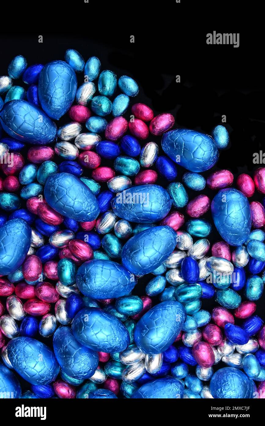 Petits et grands œufs de pâques en papier d'aluminium rose, bleu et argent, sur fond noir. Banque D'Images