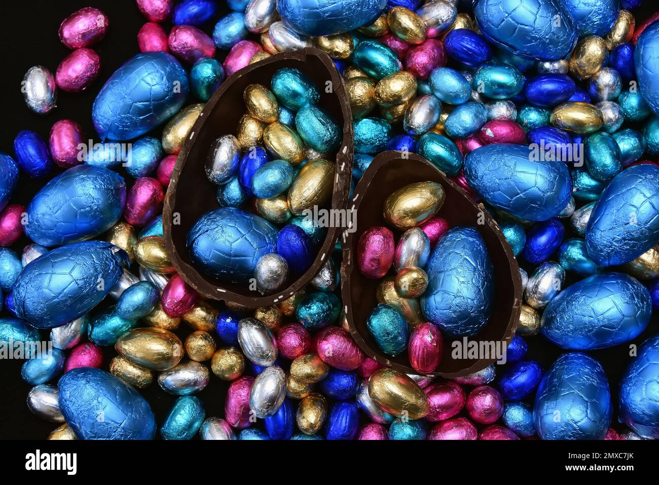 Pile de plusieurs couleurs et de différentes tailles d'oeufs de pâques au chocolat enveloppés d'une feuille colorée en bleu, rose, argent et or. Banque D'Images