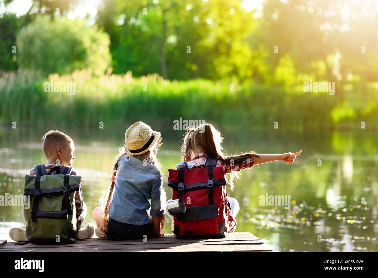 Vacances scolaires. Groupe d'enfants assis sur une jetée en bois près de la rivière Banque D'Images