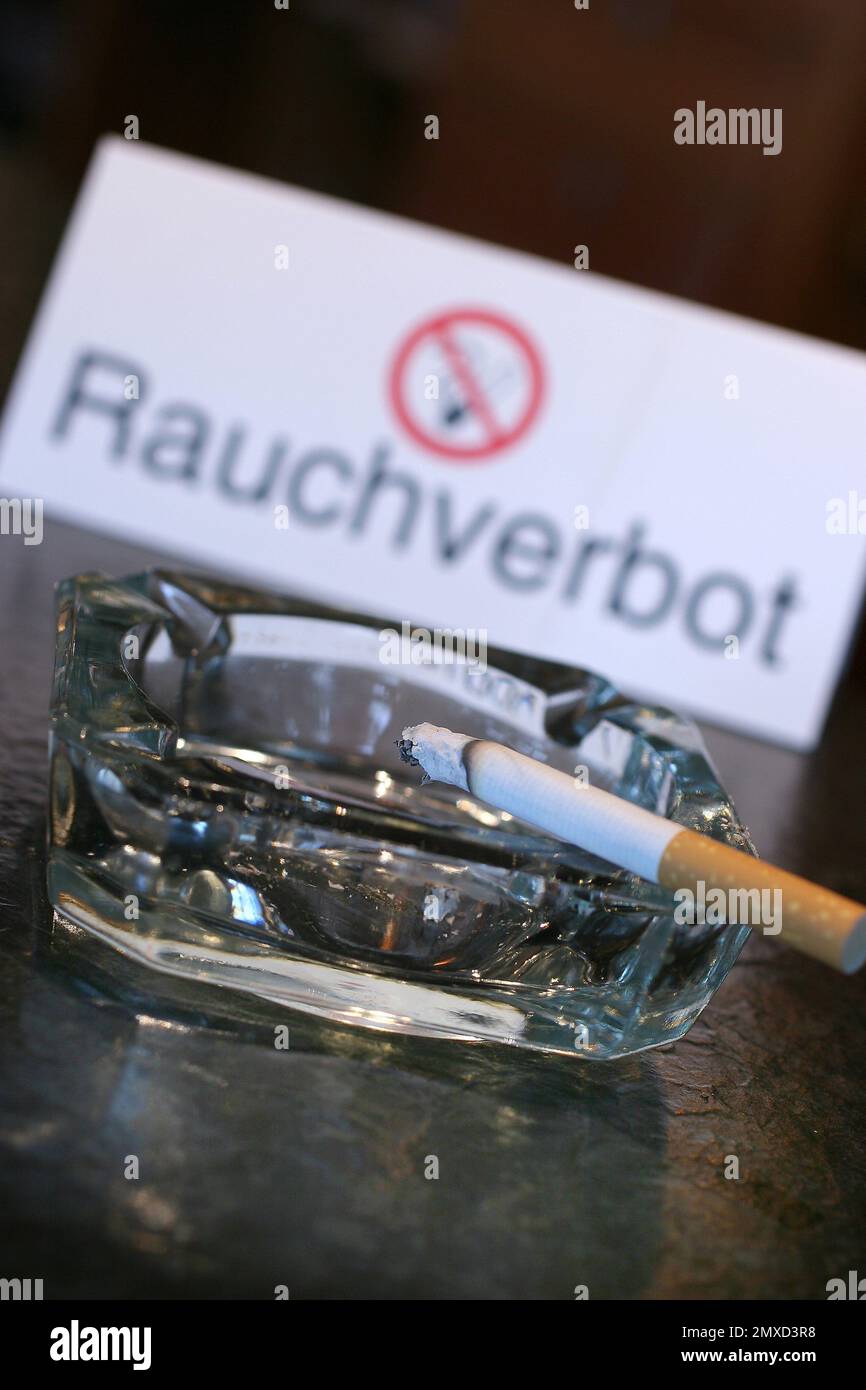 Cigarette couvant dans un cendrier devant un panneau 'Rauchverbot' Banque D'Images
