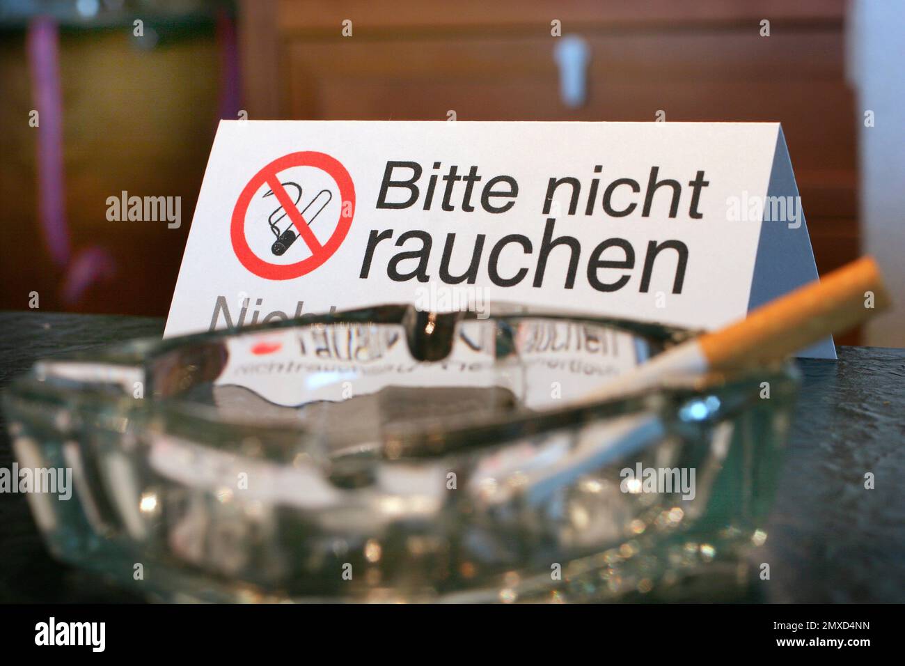 Cigarette dans un cendrier devant le panneau 'Bitte nicht rauchen Nichtrauchertisch' Banque D'Images
