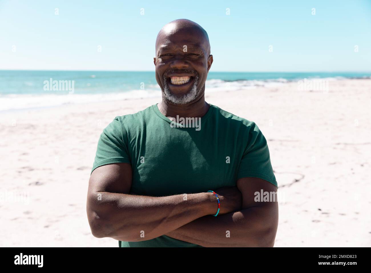 Portrait d'un homme senior afro-américain aux bras croisés souriant et debout contre la mer et le ciel Banque D'Images