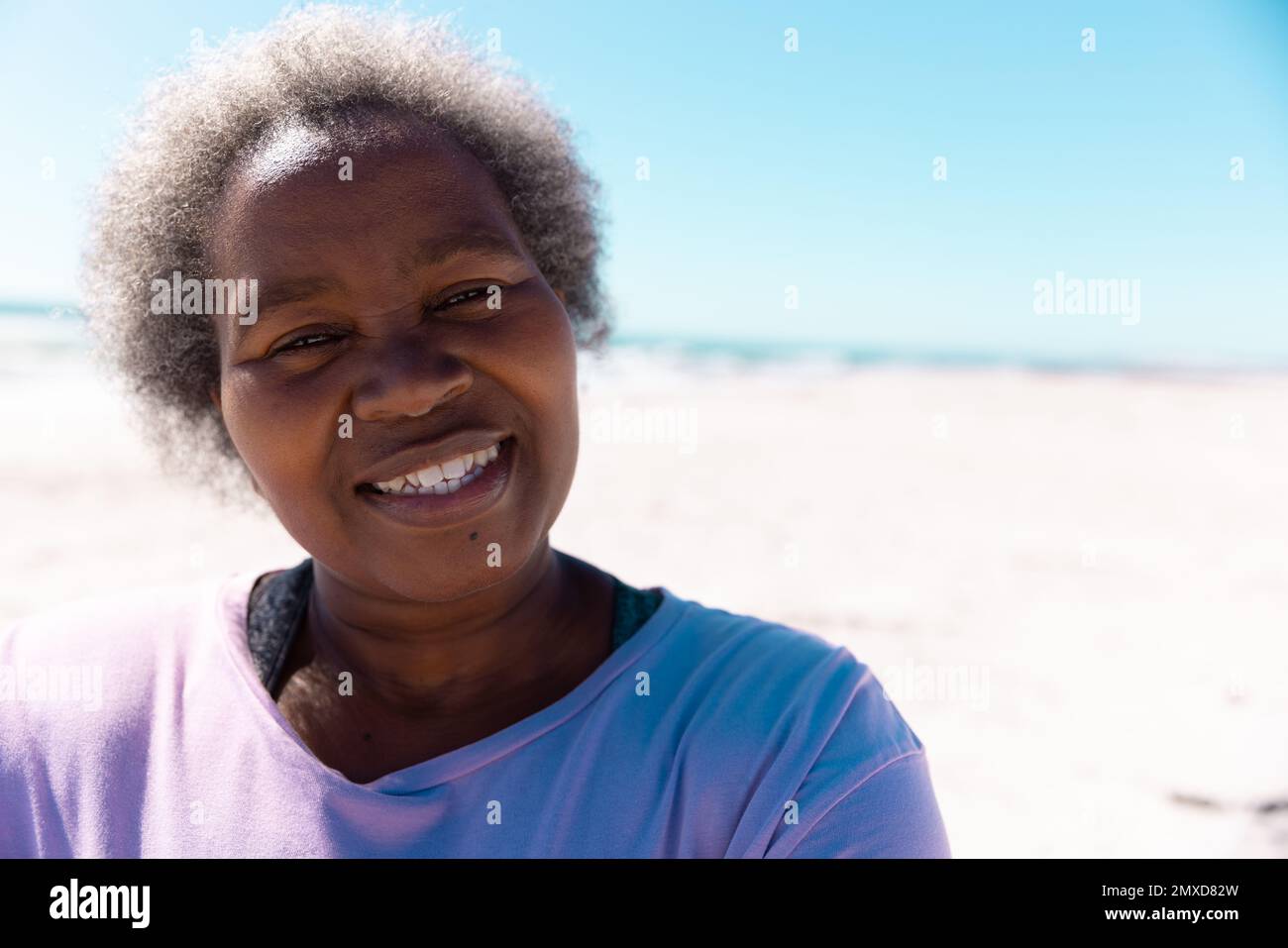 Portrait rapproché d'une femme afro-américaine âgée aux cheveux gris courts souriant sur une plage de sable Banque D'Images