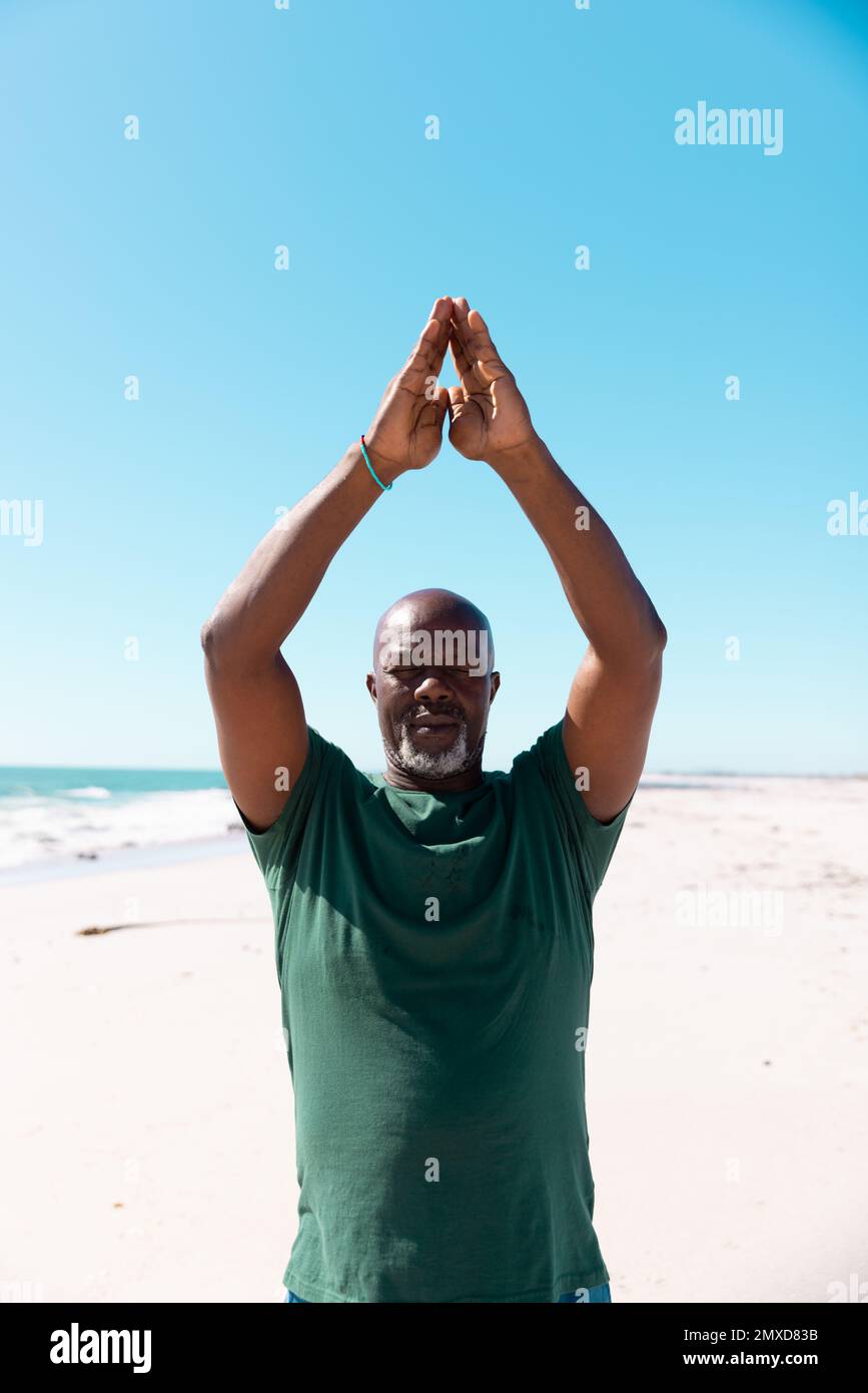 Homme âgé chauve d'Amérique d'Afrique avec des armes levées méditant à la plage sous ciel clair le jour ensoleillé Banque D'Images