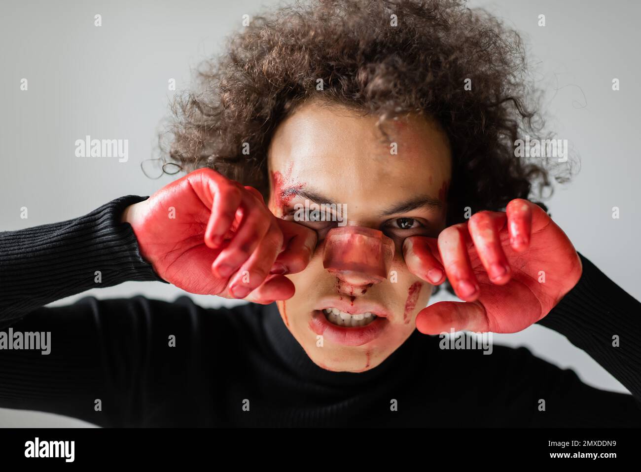 blessé afro-américain tenant les mains sanglantes près du visage avec le nez cassé isolé sur gris, image de stock Banque D'Images