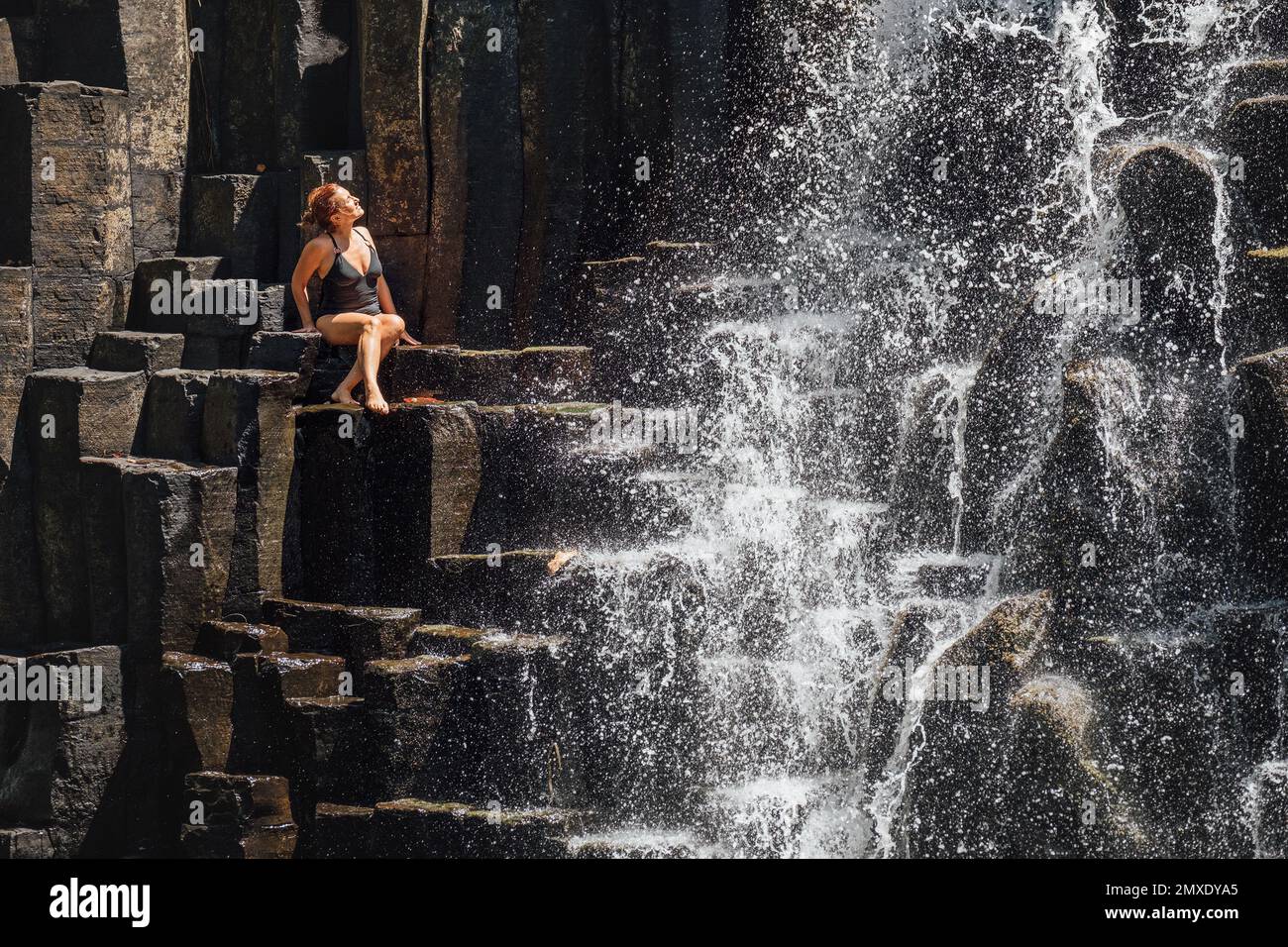 Femme caucasienne en maillot de bain noir appréciant les ruisseaux d'eau tombant sur des cascades de pierre volcanique noire. Chutes d'eau de Rochester - populaire tou Banque D'Images