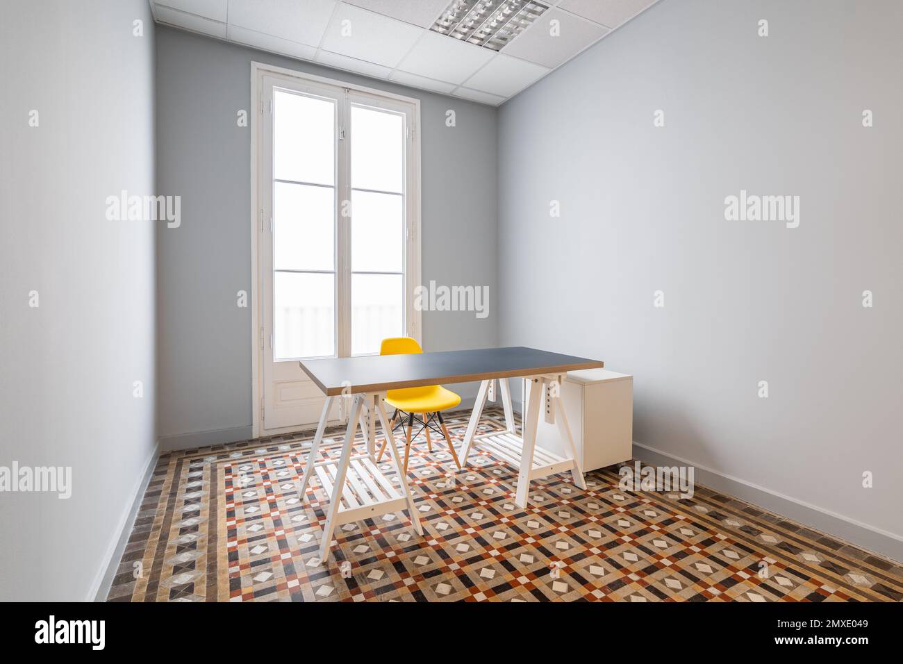 Une chambre vide avec des murs gris lisses, des portes menant à la terrasse. Le sol est fait de carreaux de marbre à motifs. Il y a une table avec un dessus gris et un plastique jaune Banque D'Images