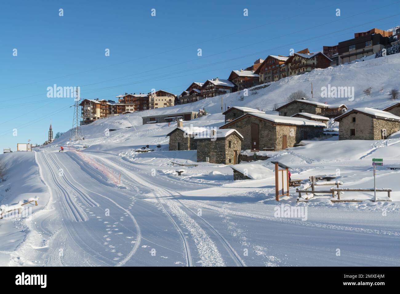 Chalets et granges en pierre le long d'une piste de ski dans la station de ski alpin française des Menuires par un matin winer lumineux et ensoleillé avec beaucoup de neige fraîche. Banque D'Images