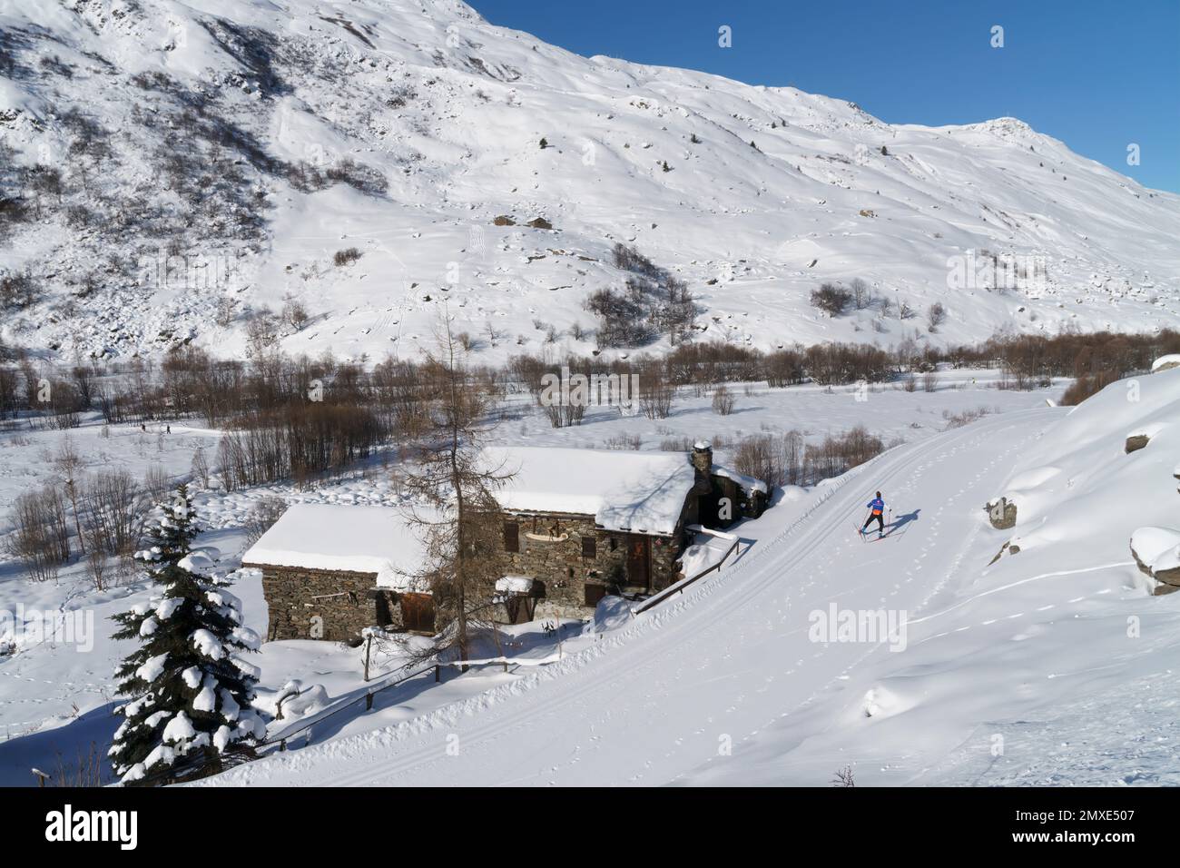 Un skieur de fond sur une piste à côté d'une maison traditionnelle en pierre près de la station de ski des Menuires dans le domaine skiable des 3 Vallées dans les Alpes françaises. Banque D'Images
