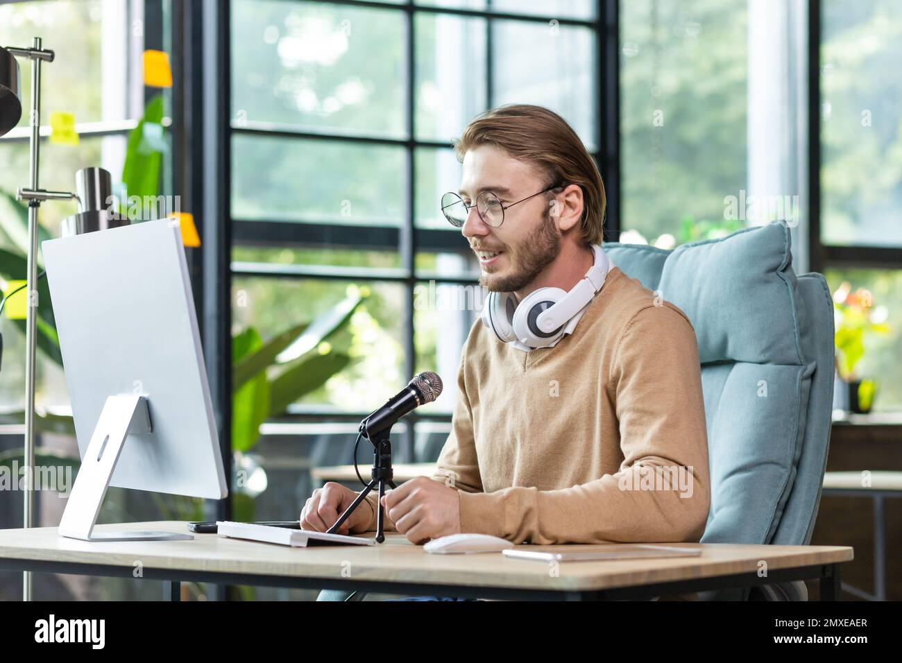 Jeune homme blogueur élégant assis au bureau dans le bureau à l'ordinateur  devant le microphone. Enregistre un podcast, parle lors d'un appel vidéo,  communique dans une discussion en ligne Photo Stock -
