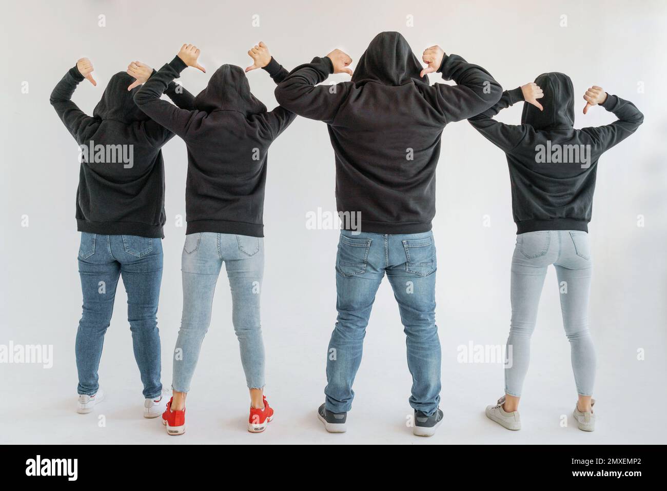 Trois femmes et un homme dans les vêtements de compagnie avec des sweats à capuche noirs et des jeans se tiennent avec leur dos au spectateur sur un fond blanc. Tout le monde a Banque D'Images