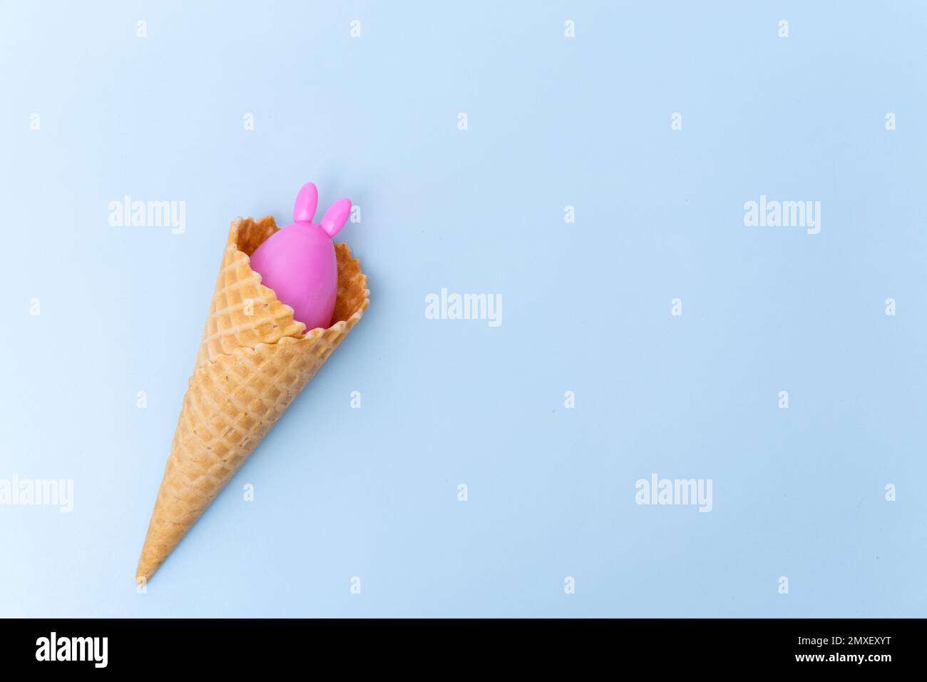 Un cornet de crème glacée gaufrée avec un œuf de Pâques rose caché avec des oreilles comme un lapin sur fond bleu, concept, espace de copie, plat. Pâques minimaliste gr Banque D'Images