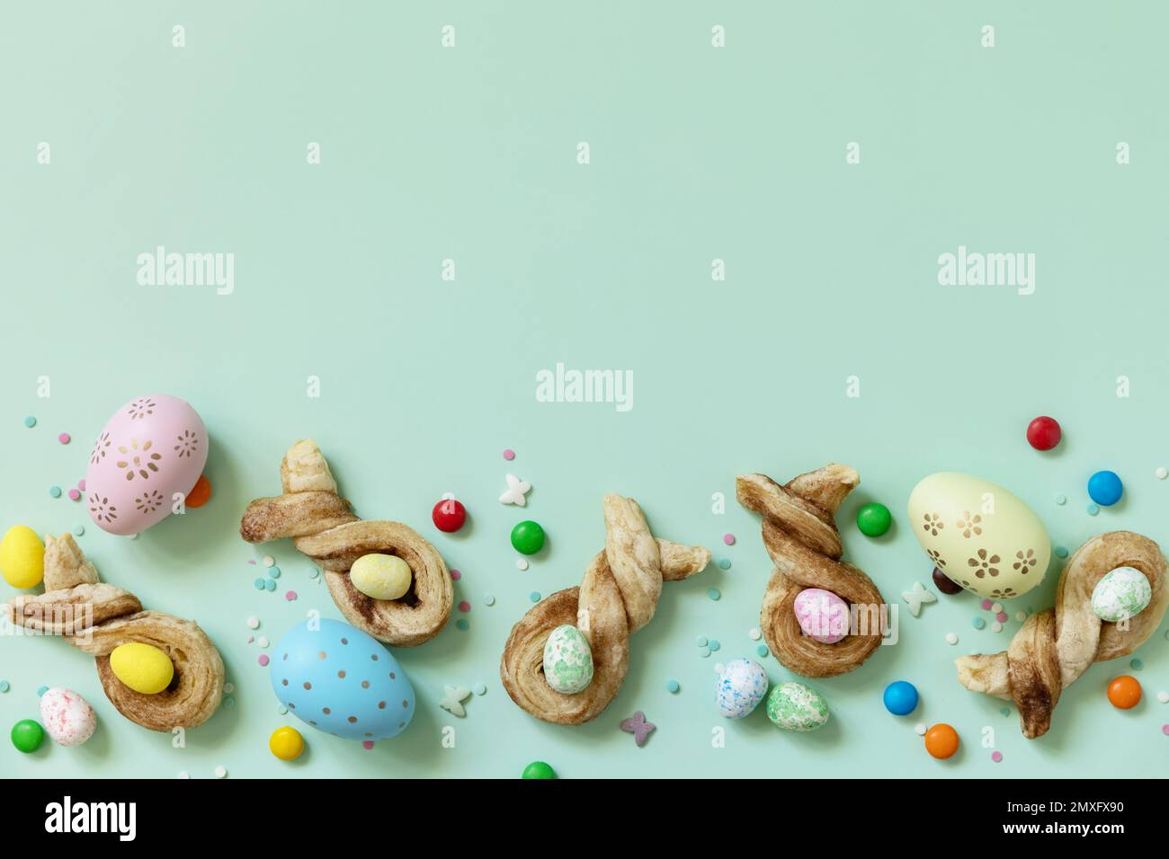 Colore les œufs de Pâques avec des petits pains en forme de lapin de Pâques, pâte feuilletée à la cannelle sur fond vert pastel. Joyeuses Pâques. Vue de dessus. Copie s Banque D'Images