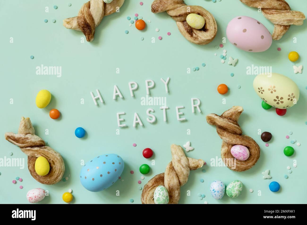 Joyeuses Pâques. Colore les œufs de Pâques avec des petits pains en forme de lapin de Pâques, pâte feuilletée à la cannelle sur fond vert pastel. Vue de dessus. Banque D'Images