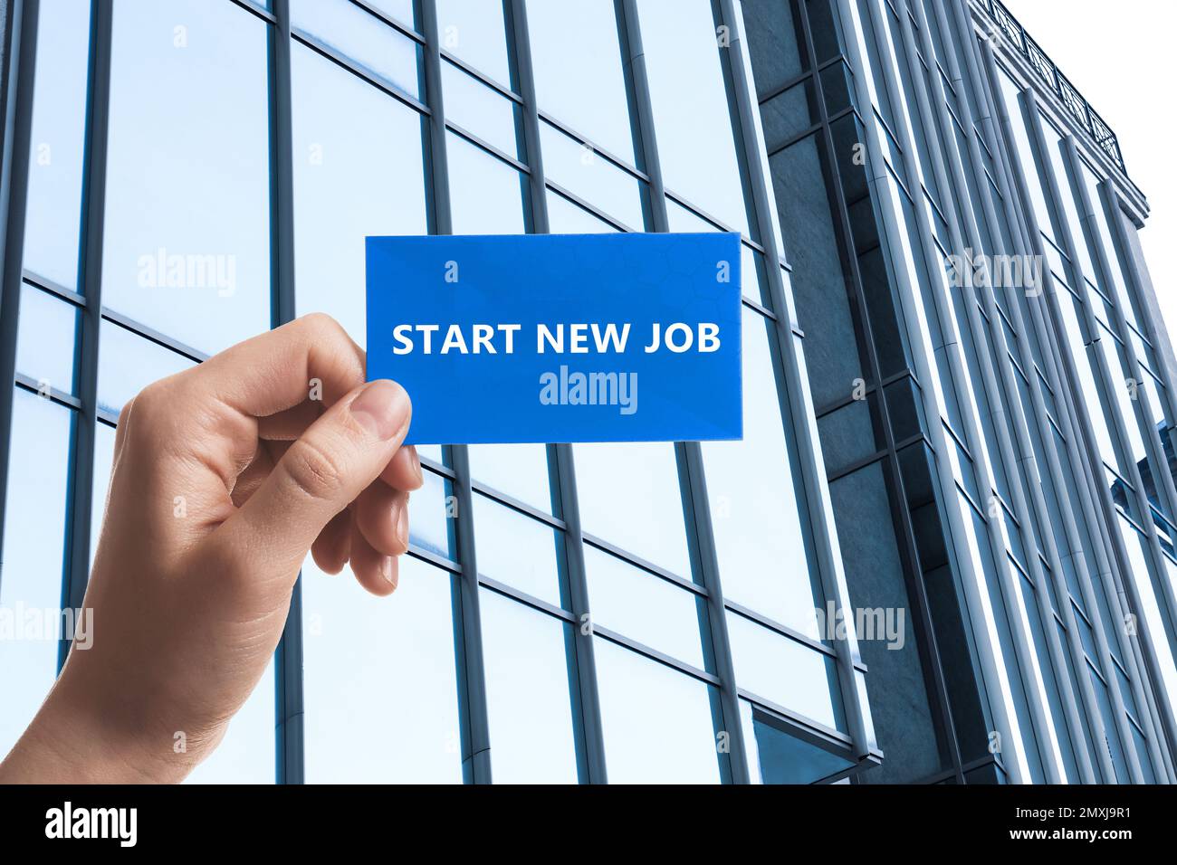 Changez votre vie. Femme tenant la carte avec le texte commencer un nouvel emploi contre le bâtiment moderne, fermer Banque D'Images