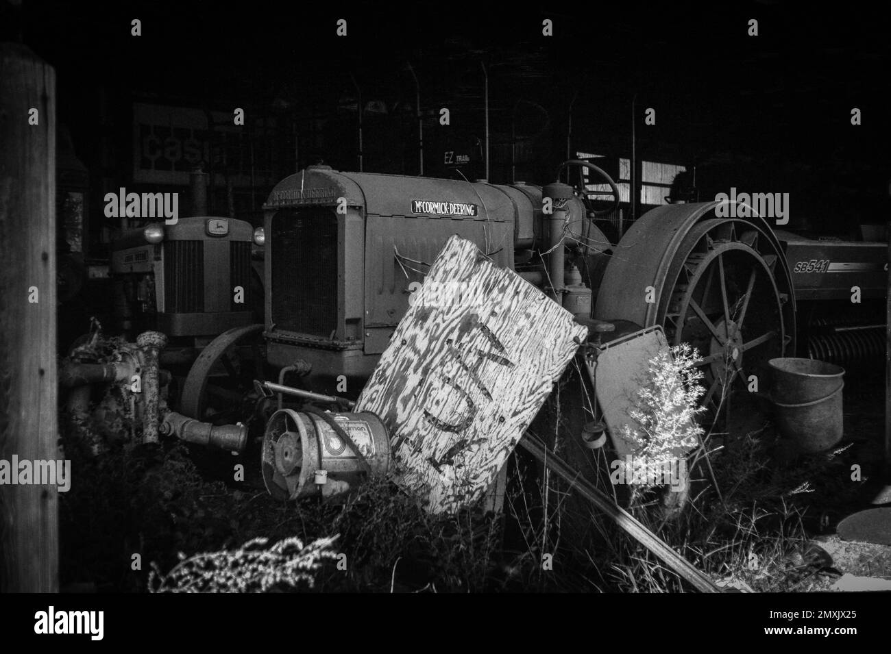 Les tracteurs McCormick Deering et John Deere stationnés dans une grange entourée de détritus sur une ferme. Littleton, Massachusetts. L'image a été capturée en noir analogique Banque D'Images