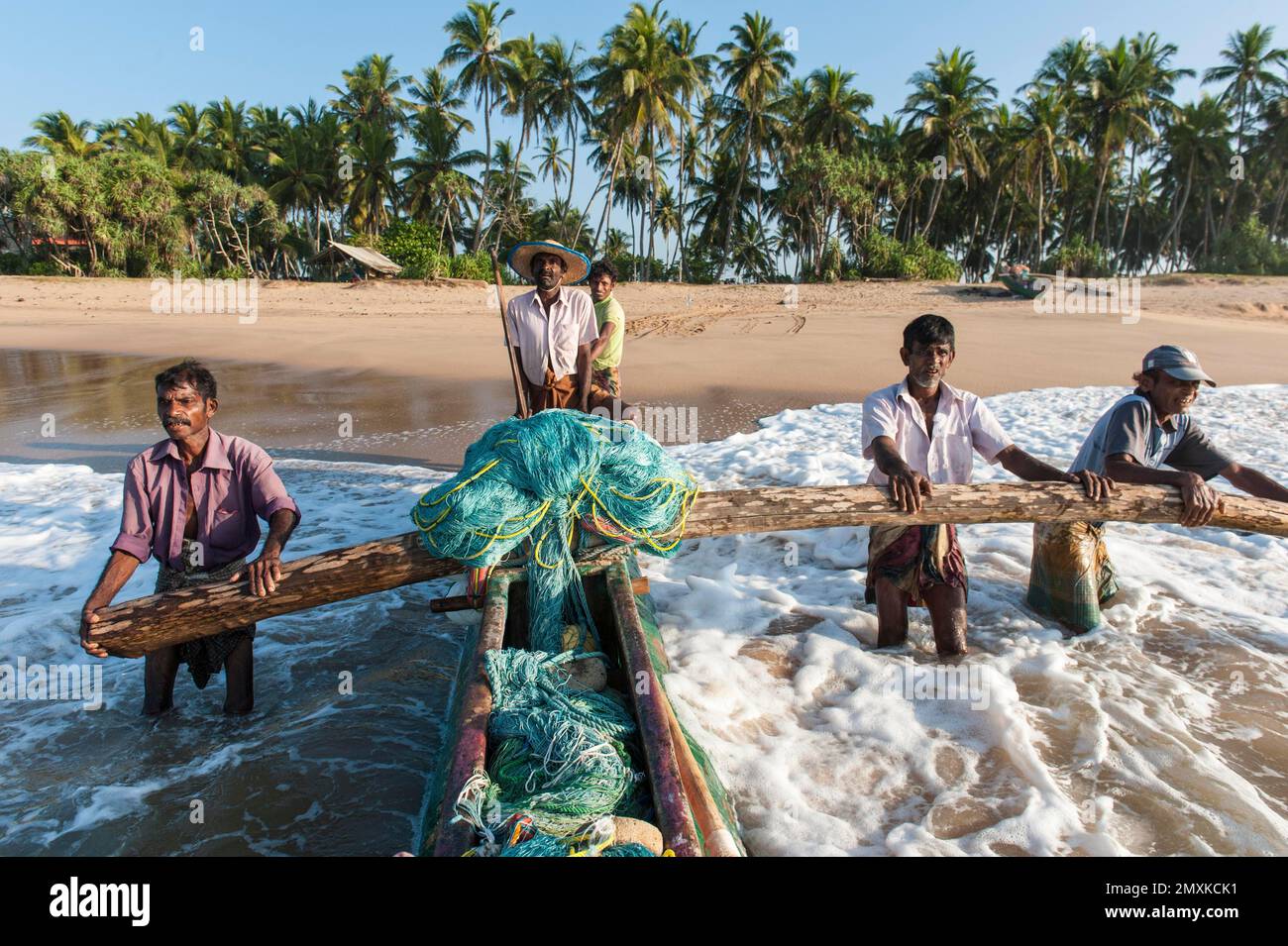 Pêcheurs au travail, pêcheurs poussant le bateau de pêche de la plage de sable dans la mer, pirogue à l'outrigger, Darwins Beach, Wella Odaya près de Ranna, S Banque D'Images