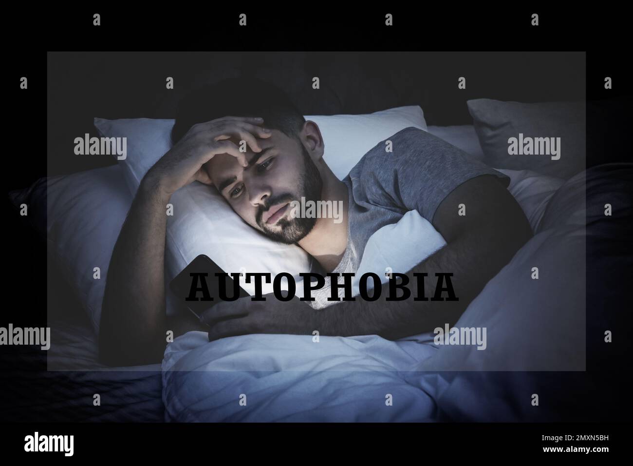 Jeune homme déprimé avec un smartphone dans le lit la nuit. Autophobie - peur de l'isolement Banque D'Images