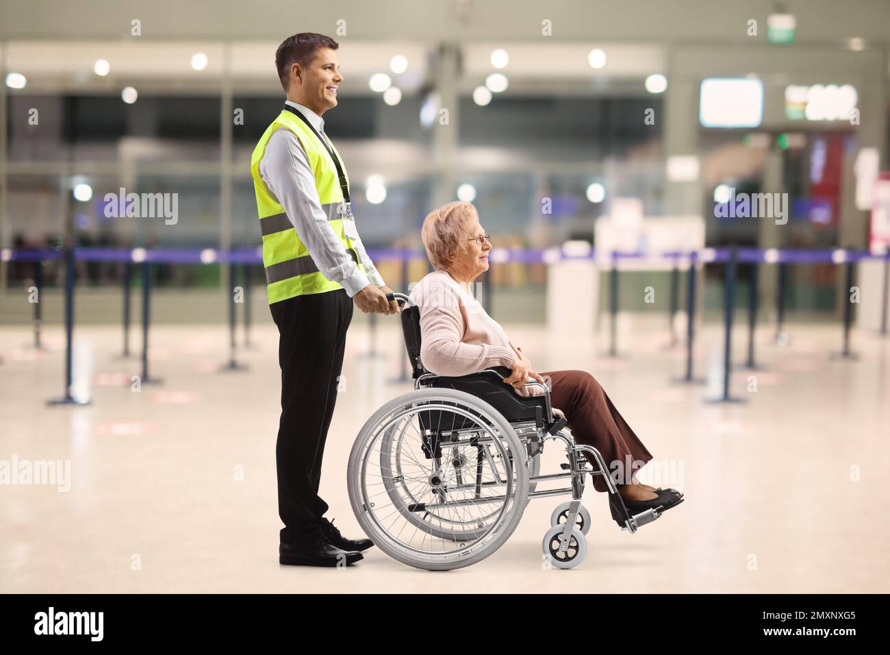 Assistant aidant une femme âgée en fauteuil roulant à l'aéroport Banque D'Images