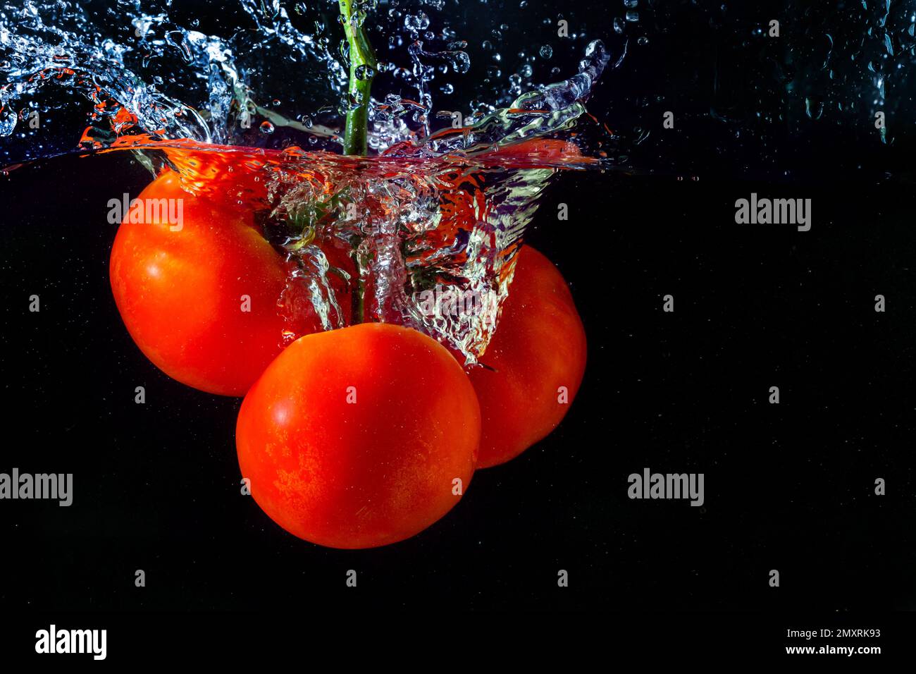 Tomate rouge fraîche tombant dans l'eau avec des éclaboussures d'eau et des bulles d'air isolées sur fond noir. Banque D'Images