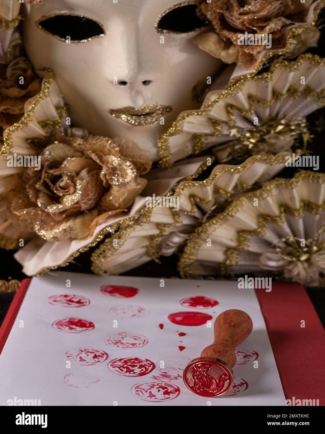 Un timbre avec la figure d'un chat est utilisé sur une feuille blanche à l'encre rouge et avec un masque de carnaval en arrière-plan Banque D'Images