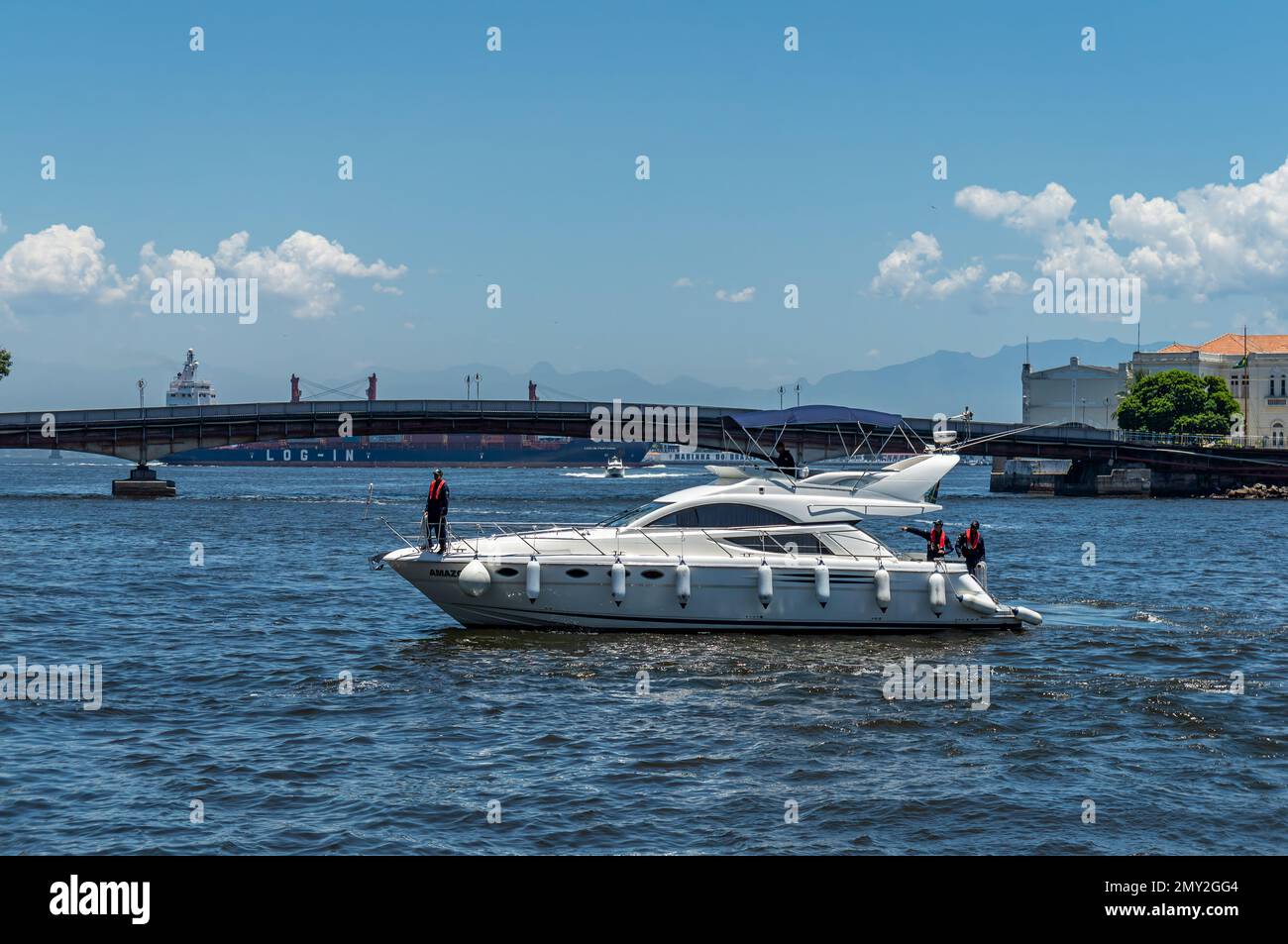 Un hors-bord blanc naviguant sur les eaux de la baie de Guanabara, à proximité de l'embarcadère de Sao Bento et du pont Arnaldo Luz à l'arrière, sous un ciel bleu clair et ensoleillé. Banque D'Images