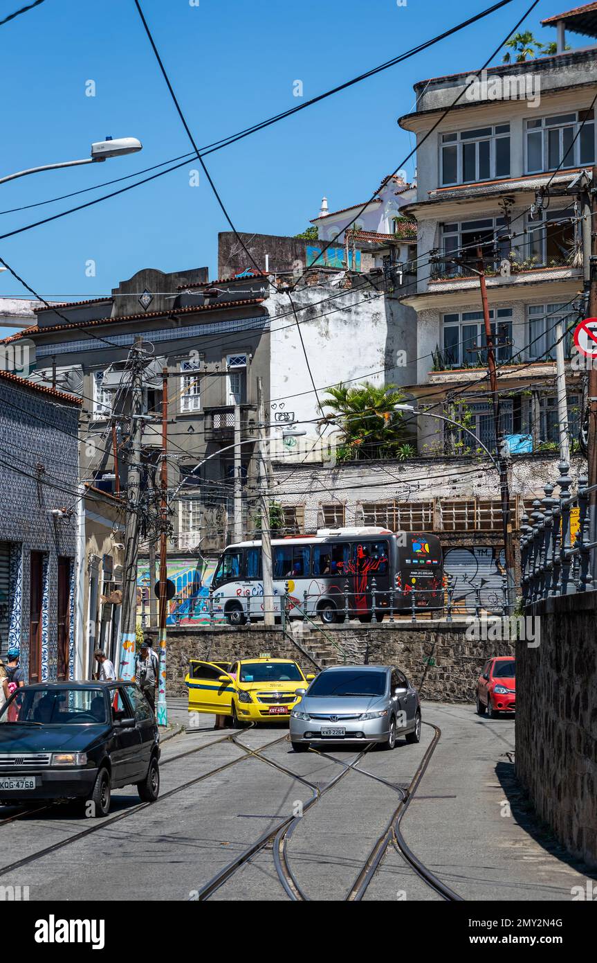 Circulation passant par la rue Almirante Alexandrino dans le quartier de Santa Teresa entre les anciens bâtiments près de l'arrêt de tram sous ciel bleu clair ensoleillé d'été. Banque D'Images
