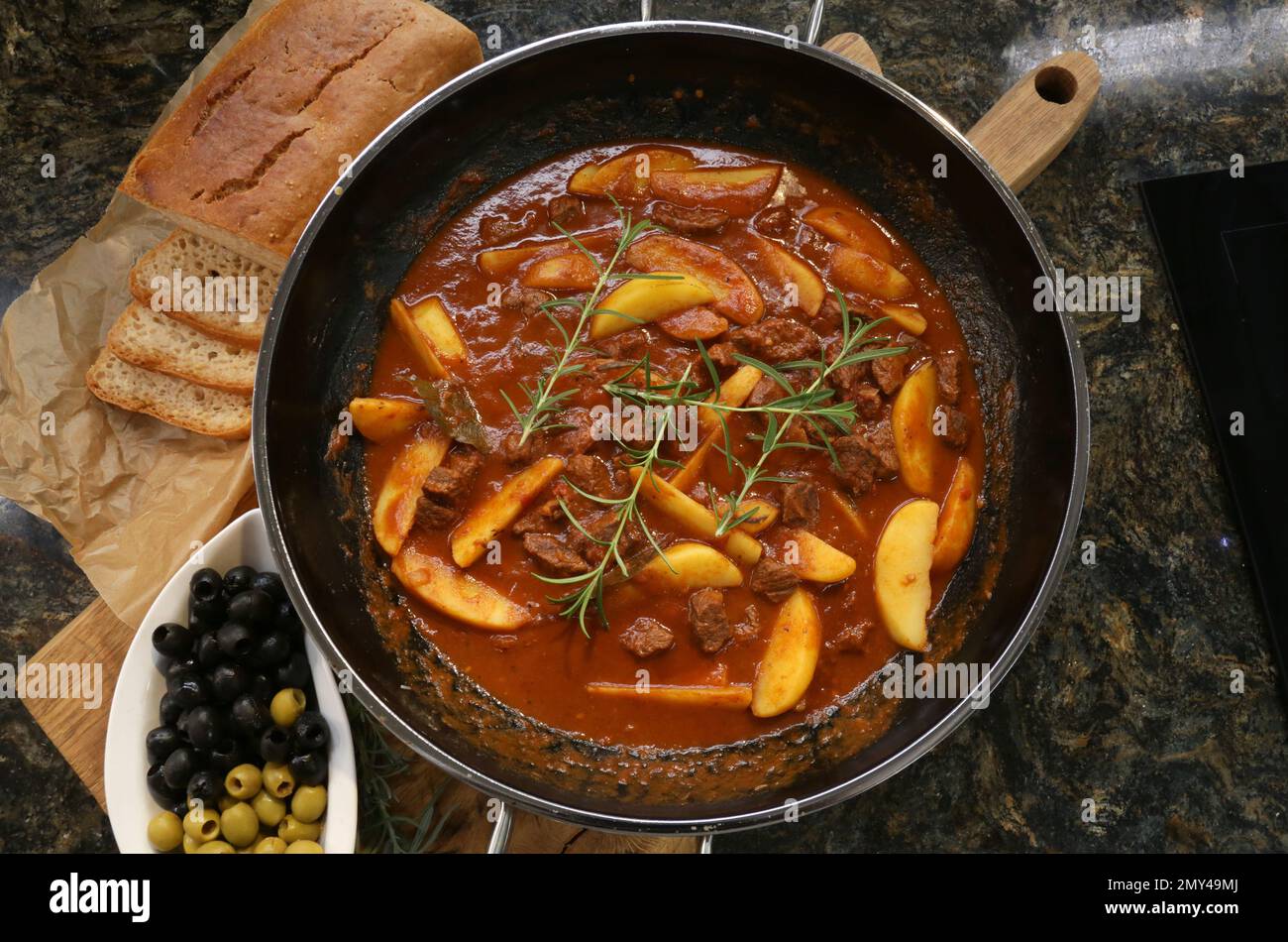 Bœuf braisé dans une sauce au vin rouge servi avec des pommes de terre cuites au four, du pain, des olives et du romarin. Banque D'Images