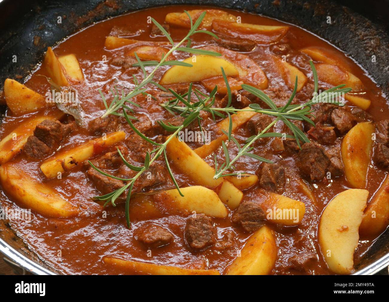 Bœuf braisé dans une sauce au vin rouge servi avec des pommes de terre cuites au four, du pain, des olives et du romarin. Banque D'Images