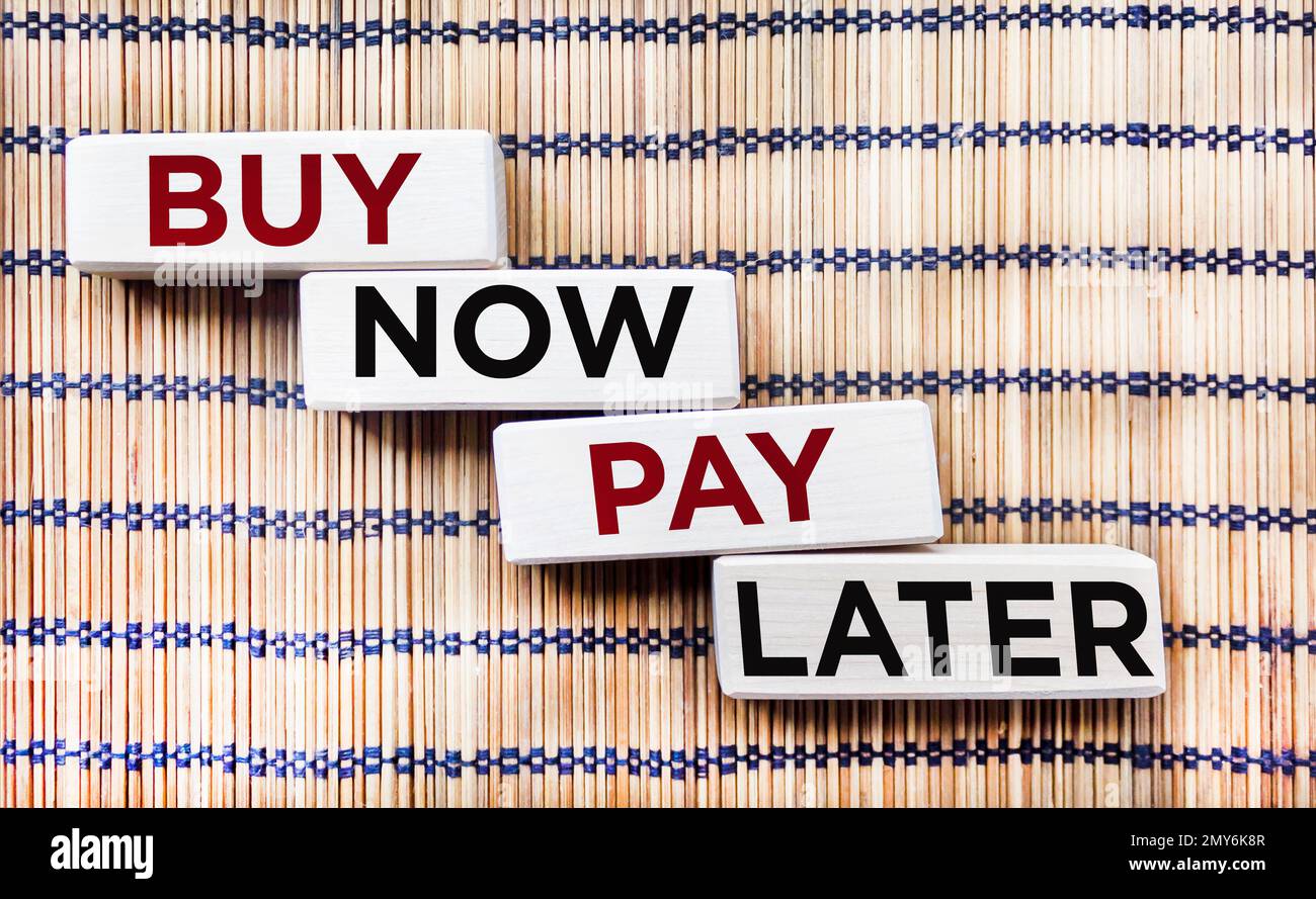 Sur un beau fond sont quatre blocs de bois avec les mots ACHETER MAINTENANT, PAYER PLUS TARD. Banque D'Images