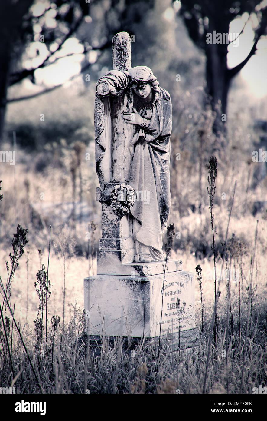 Une échelle de gris verticale d'une statue d'une femme en deuil qui embrasse la croix sur la tombe Banque D'Images