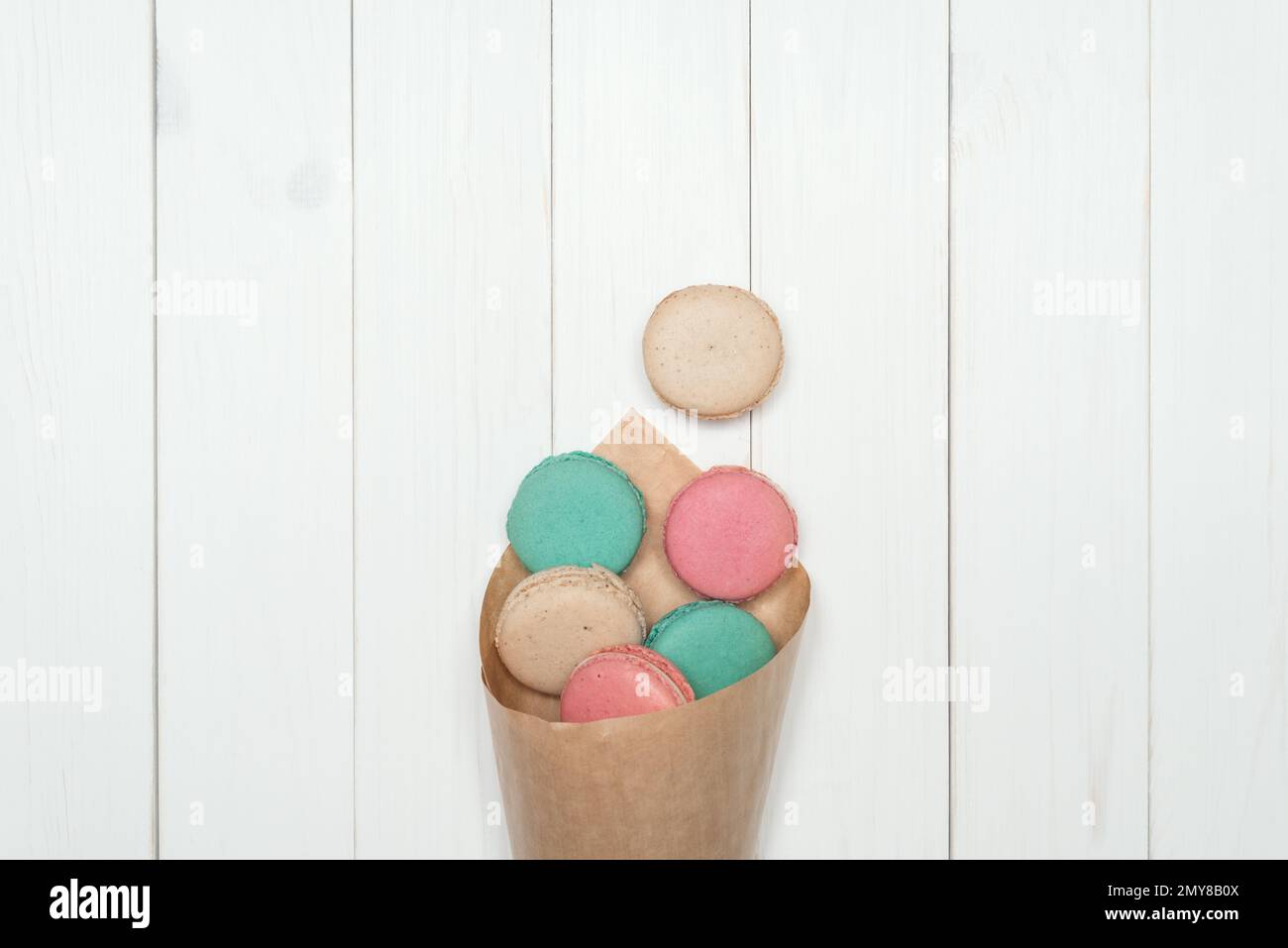 Sacs en papier avec biscuits macaron couleurs différentes. Délicieux dessert français sur fond de bois blanc. Modèle pour la conception. Mise en page à plat, vue de dessus Banque D'Images