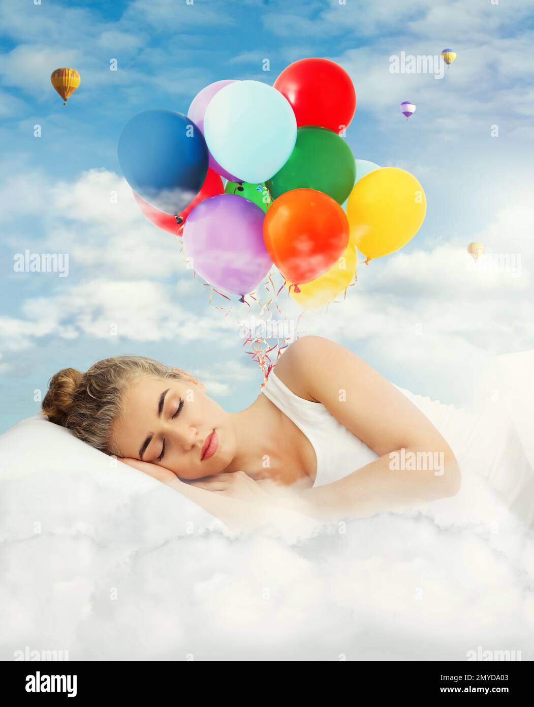 Jeune belle femme dormant dans le lit. Ballons d'air lumineux dans un ciel bleu nuageux - doux rêves Banque D'Images