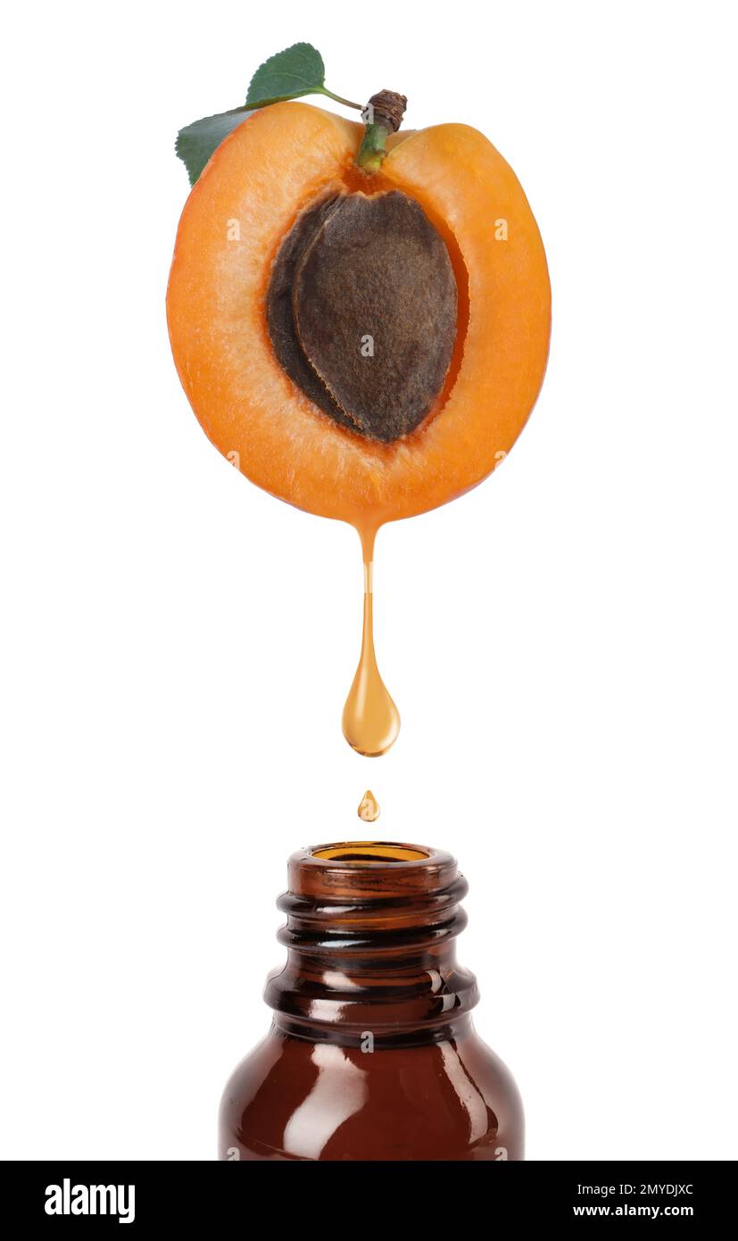 L'huile de grains d'abricot s'égoutte de la moitié des fruits frais dans une bouteille de verre sur fond blanc Banque D'Images