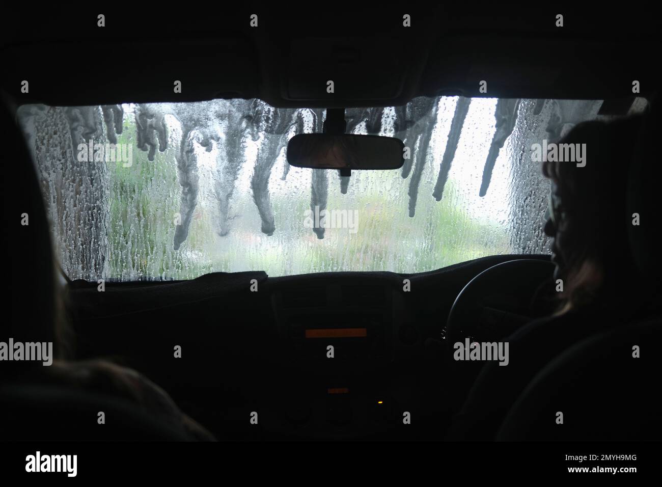 Vue de l'intérieur d'une voiture lorsqu'elle traverse un lave-auto automatique, pare-brise humide. Banque D'Images