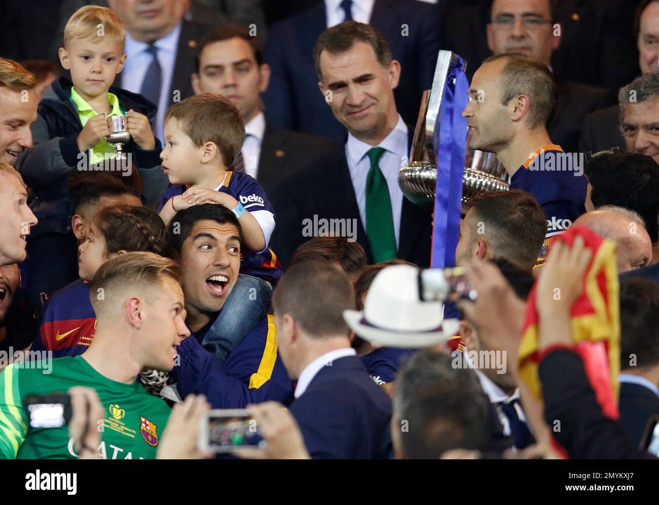 Barcelona's Luis Suarez, center left, smiles carrying a child while in the background Spain's King Felipe hands the trophy to team captain Andres Iniesta after they won the final of the Copa del Rey soccer match between FC Barcelona and Sevilla FC at the Vicente Calderon stadium in Madrid, Sunday, May 22, 2016. Barcelona won 2-0. (AP Photo/Daniel Ochoa de Olza) Banque D'Images