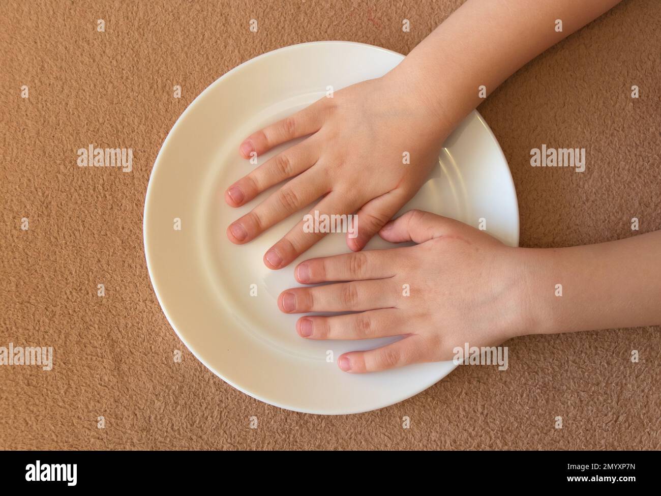 les petites mains des enfants se trouvent dans une assiette vide sur la table Banque D'Images